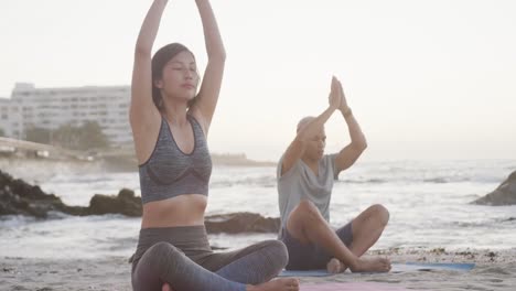 happy biracial couple doing yoga and meditating at beach at sundown, in slow motion