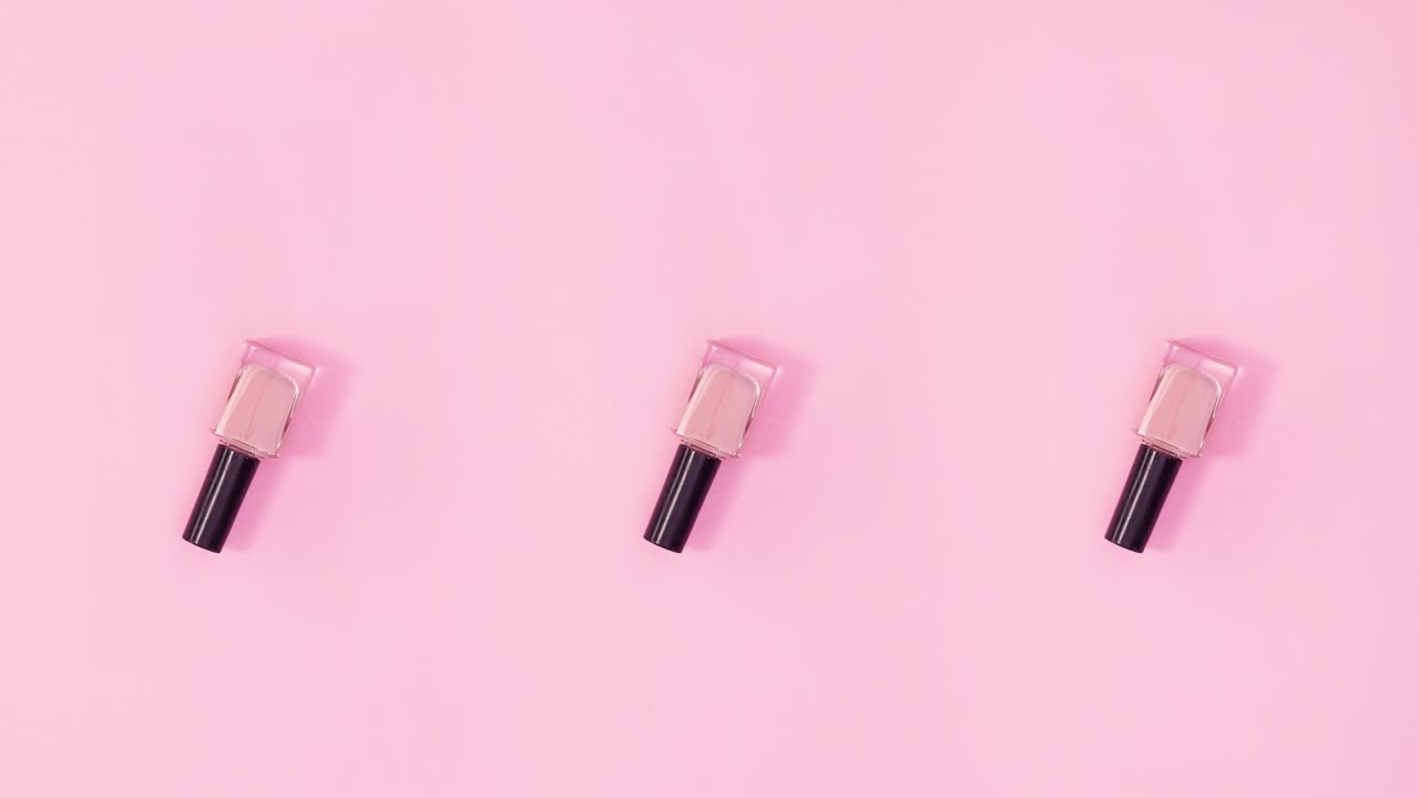 Three nail polishes bottles rotate on pastel pink background. Stop motion