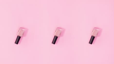 three nail polishes bottles rotate on pastel pink background. stop motion