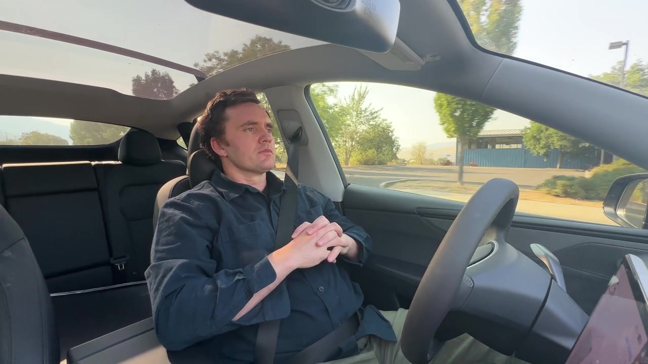 Man sits relaxed with hands clasped in his lap as his electric vehicle drives itself hands-free down a rural road.