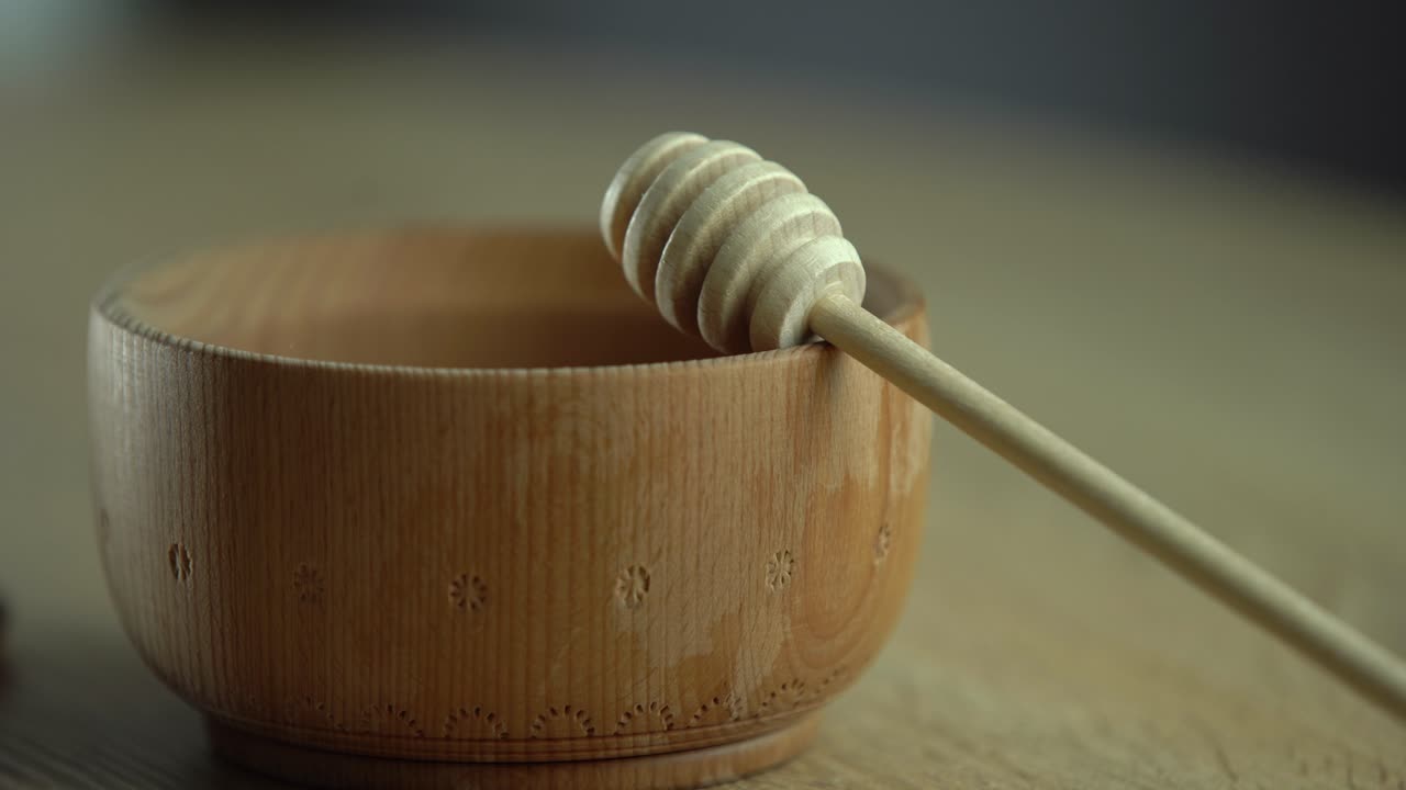 miele in una ciotola di legno profonda, piatto di legno rustico. Il cucchiaio di legno gocciola lentamente.