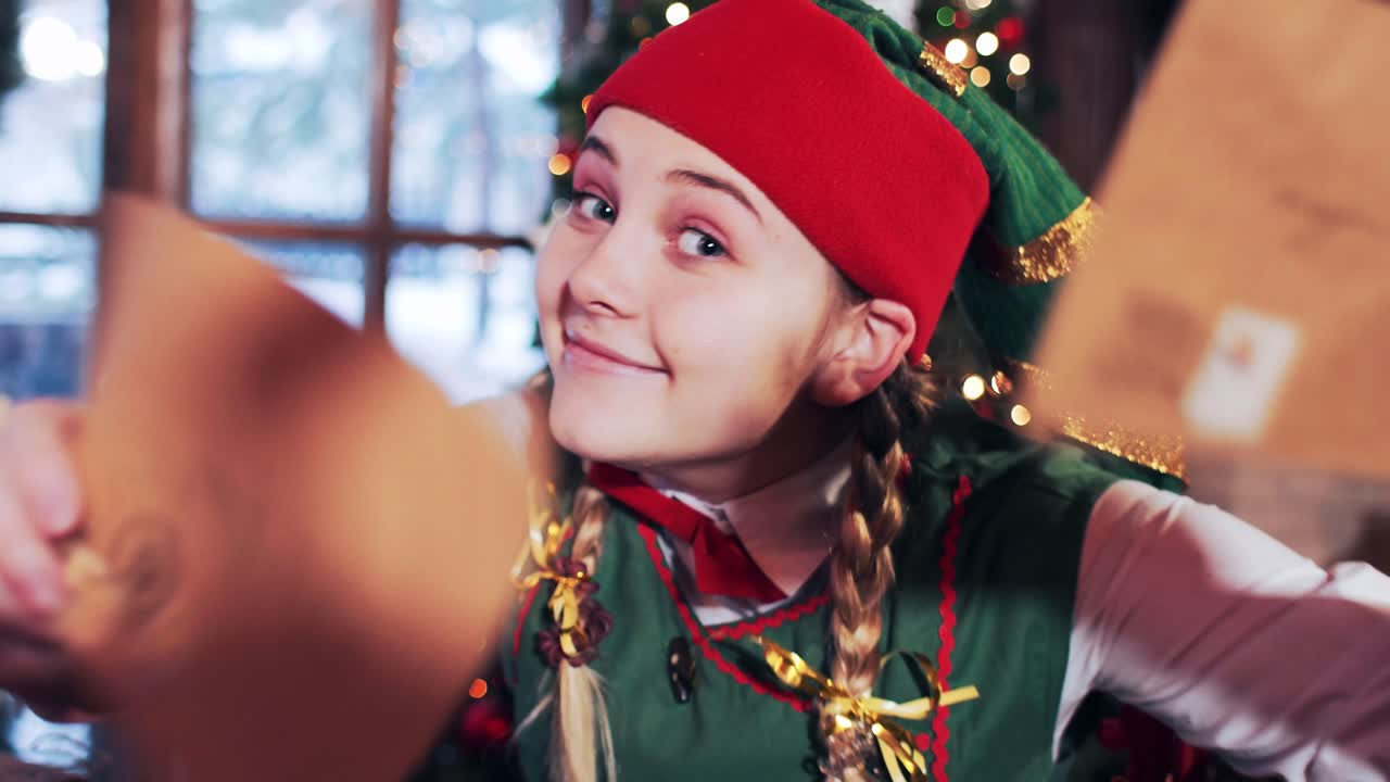 The emotions and joy of the elf girl who holds letters to Santa Claus in her hands. Room in the house with Christmas decorations and a Christmas tree