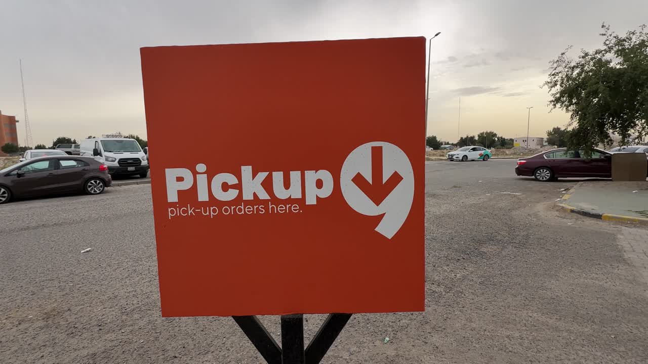 a bright pickup orders sign in an outdoor parking area near parked cars and roadside curb, showing retail order collection point in daylight