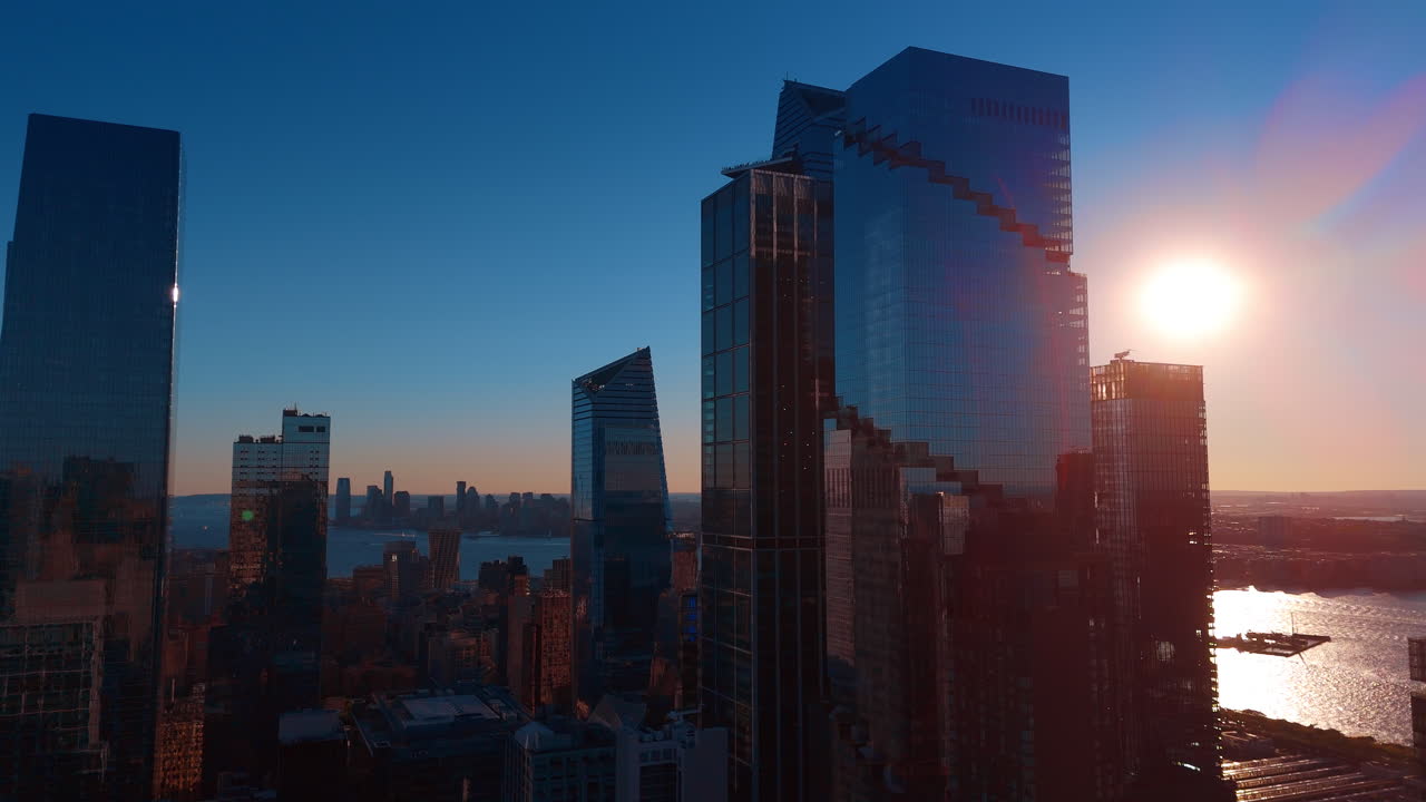 Fachada de cristal de modernos rascacielos reflejando el atardecer en una gran ciudad. Vista aérea desde un ángulo bajo de edificios contemporáneos de gran altura con ventanas de cristal que reflejan el sol brillante sobre el río.