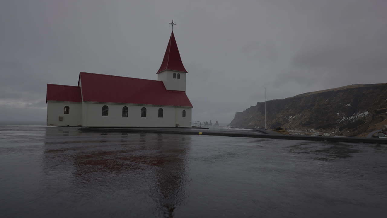 Approaching to V&iacute;k i Myrdal Church on Hill Above Sea and Coastline of Iceland on Dark Cloudy Rainy Day