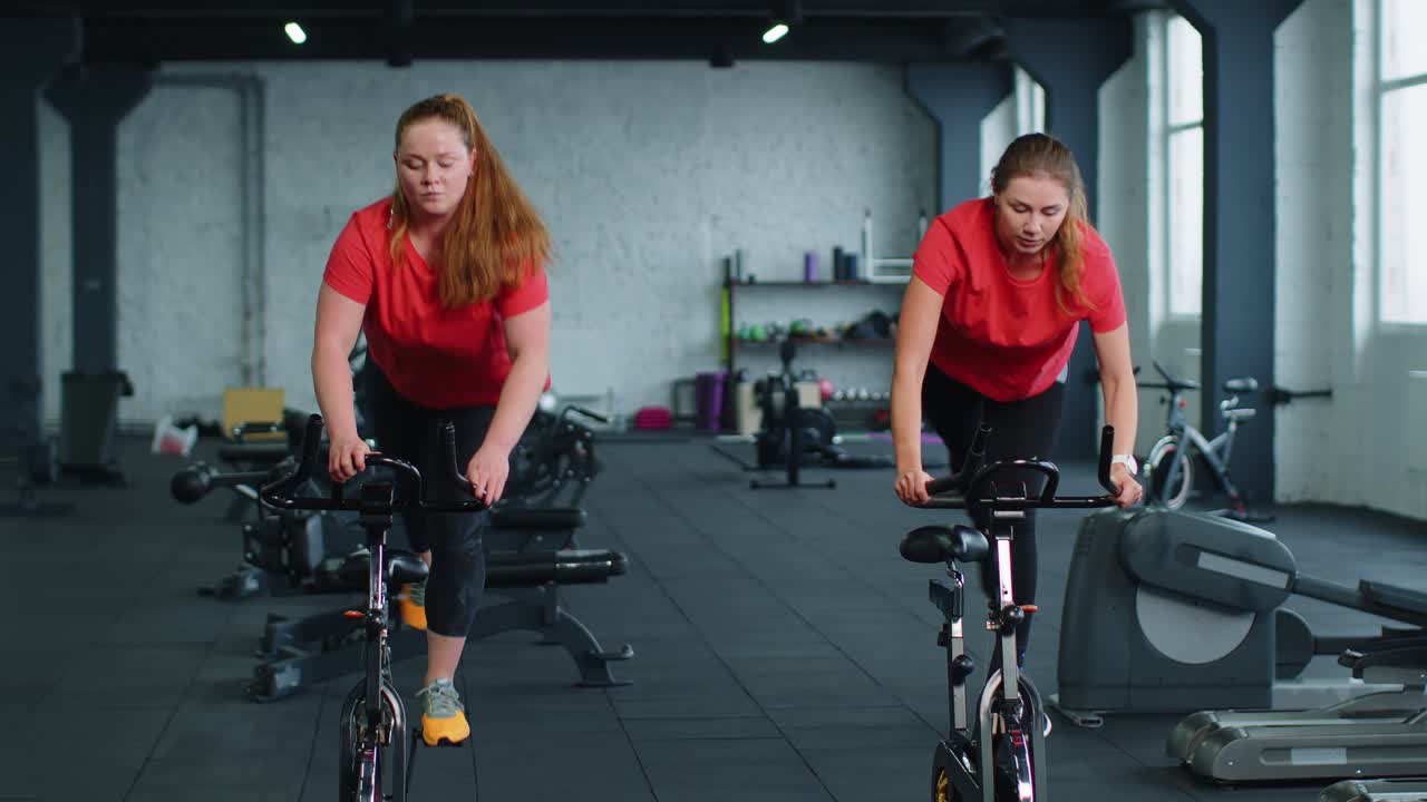 건강한 백인 여성 그룹이 체육관에서 정지 자전거 기계 자전거에서 운동을합니다.
