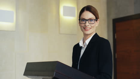 close-up view caucasian businesswoman in formal clothes and eyeglasses looking at the camera and smiling in a meeting room