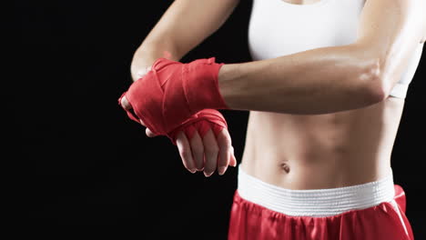 young caucasian woman boxer wraps her hands with red boxing wraps on a black background