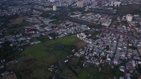 Suburbio-De-La-Ciudad-De-Ho-Chi-Minh,-Vietnam-Con-Campo-De-Arroz,-Carretera-Principal-De-La-Zona-Residencial-Y-Expansión-Urbana-Como-Se-Ve-Desde-La-Vista-Aérea-En-La-Tarde-Soleada