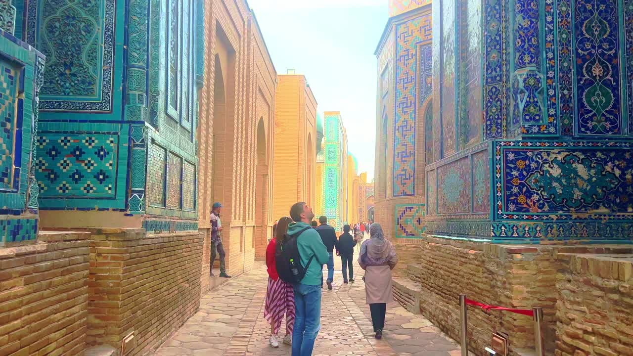 Tourists exploring the vibrant tiled architecture of the Shahi-Zinda necropolis in Samarkand, Uzbekistan