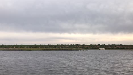 cruising past sightseeing tour boat on overcast chobe river, africa