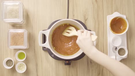 chef mixing red soup with garlic in a boiling pot, top view static