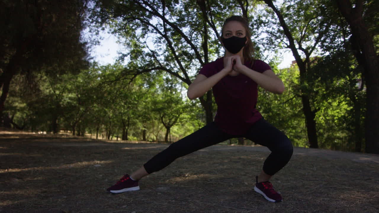 Ung kvinde iført maske laver sidelunges i en park, bredt lavvinkelbillede