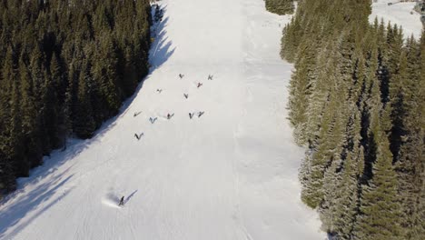 4k aerial drone of group of people skiing down a snowy mountain piste in norway surrounded by trees on a sunny day