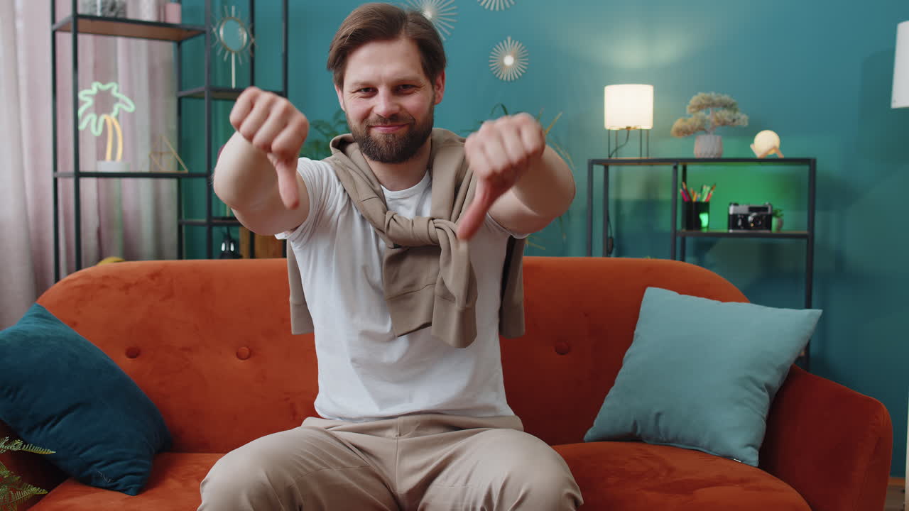 Upset caucasian man showing thumbs down dislike bad work disapproval dissatisfied feedback at home