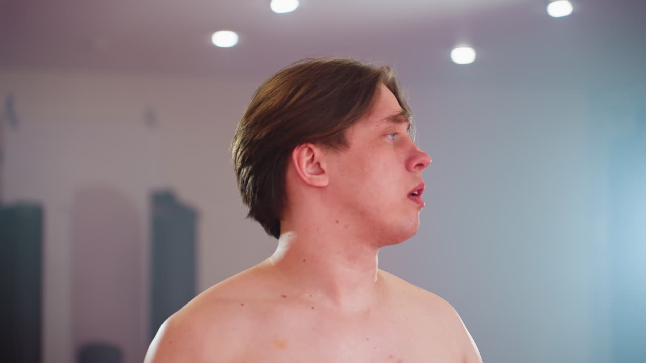 Chap lifts black shirt over head taking it off exposing bare torso in indoor setting with soft lighting, action emphasizing movement, preparation, and transition with raw authentic
