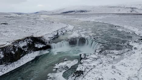 Annäherung-Aus-Der-Luft-An-Den-Wunderschönen-Godafoss-Wasserfall-In-Nordisland-An-Einem-Verschneiten-Und-Vereisten-Wintertag---Nach-Unten-Geneigte-Aufnahme-Einer-Atemberaubenden-Winterszene