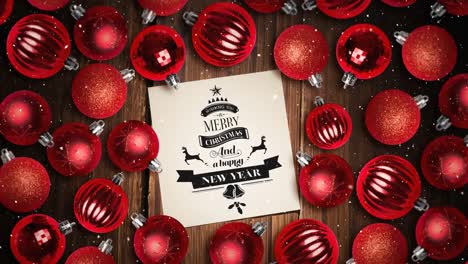 Falling-snow-and-Merry-Christmas-text-note-and-bauble-decorations-on-wood