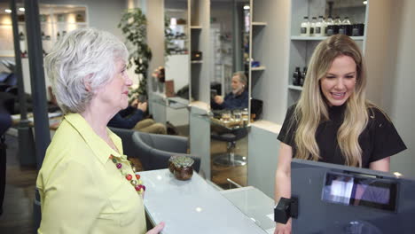 senior woman making contactless payment to stylist in salon with credit card