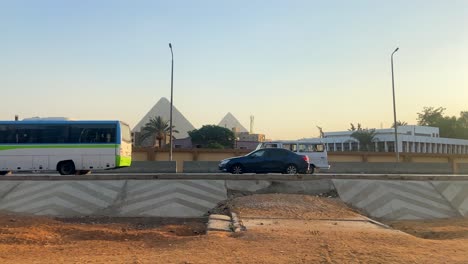 traffic driving on road in egypt at sunset, great pyramids of giza in background