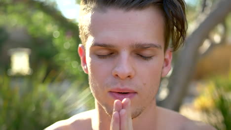 a fit young attractive white man smiling and closing his eyes in meditation and making prayer hands while focusing on present awareness, mindfulness, positivity and good vibes