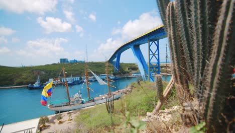 paneo lento alrededor de cactus para revelar un gran barco colombiano amarrado al lado de un río con un gran puente azul