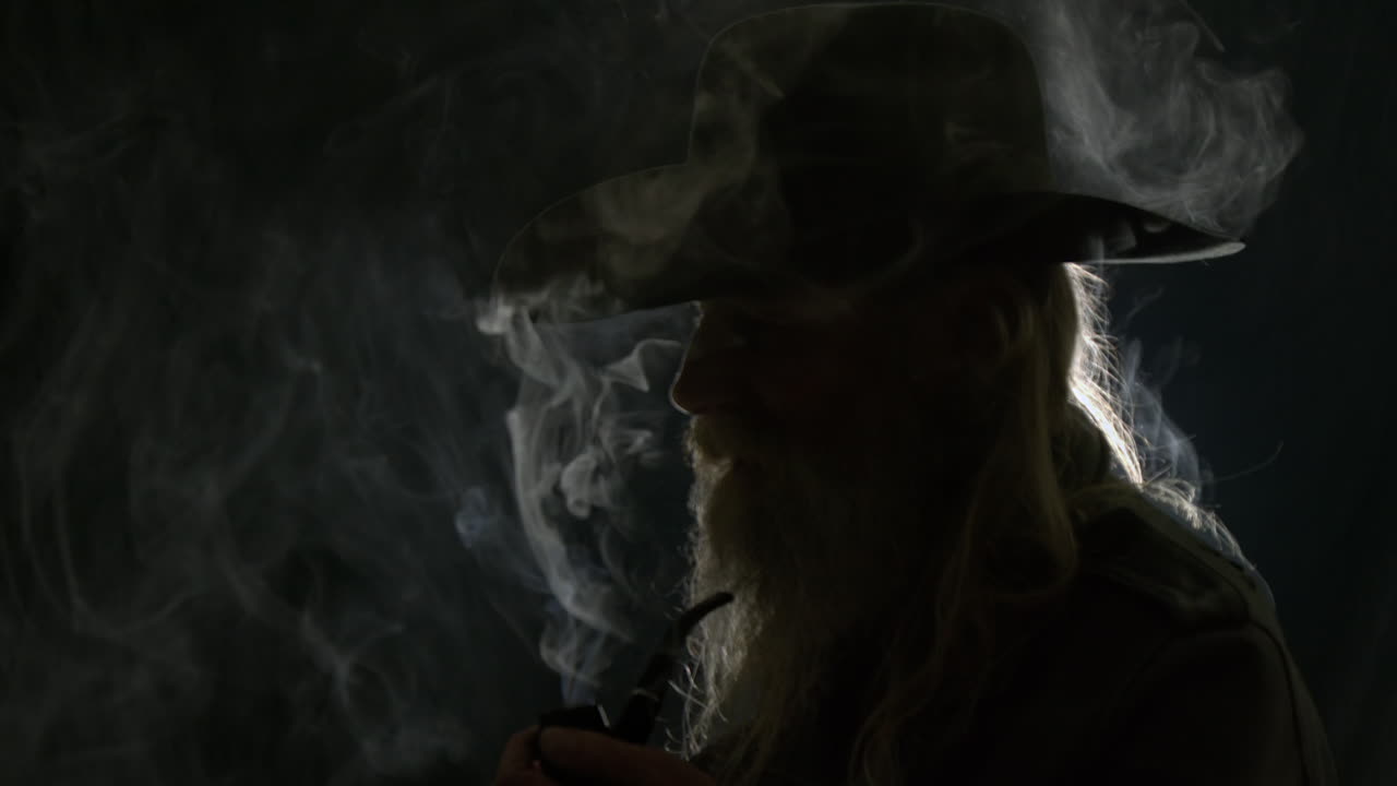 Old bearded cowboy silhouette, backlit in black room, smokes pipe