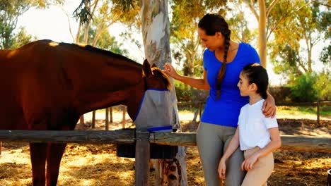 Mother-and-daughter-stroking-horse-in-ranch-4k