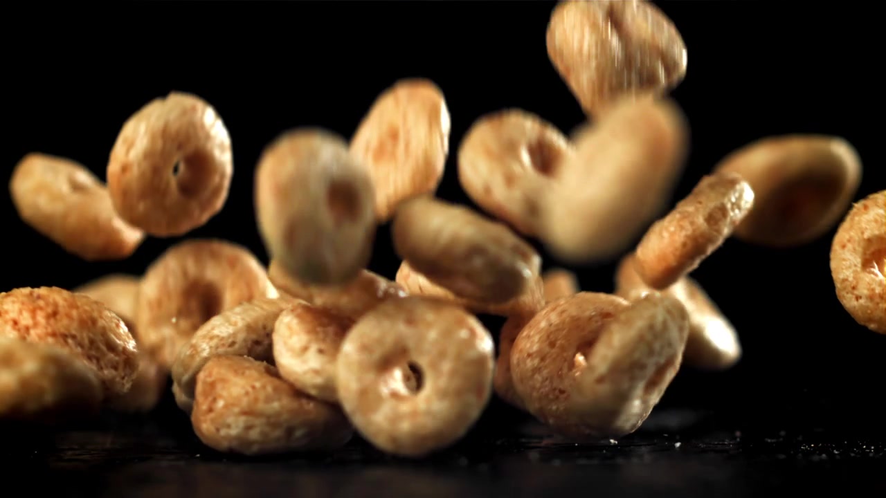Anéis de Cereal Dourados Caindo em Câmera Lenta em Fundo Preto