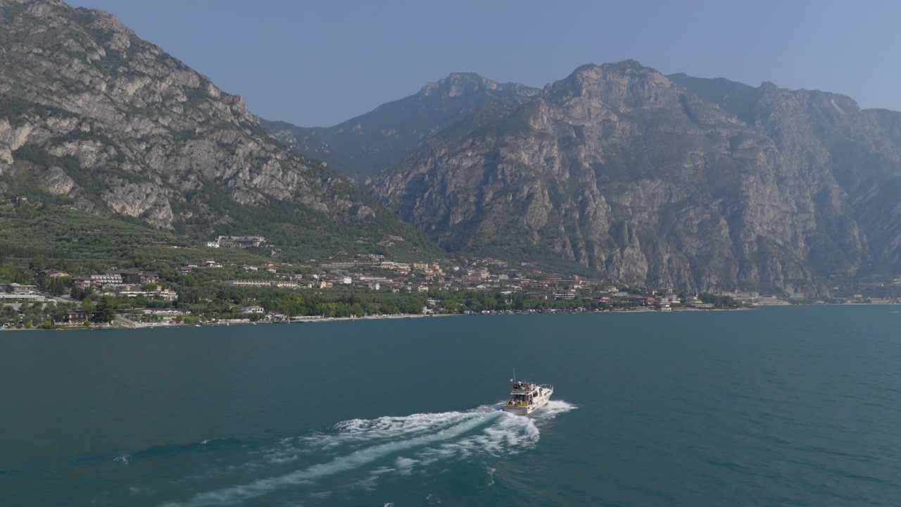 Aerial drone footage following a boat on Lake Garda near Limone sul Garda, featuring smooth panning and scenic mountain views in the background, perfect for travel and nature projects. 6k to 4k 60fps