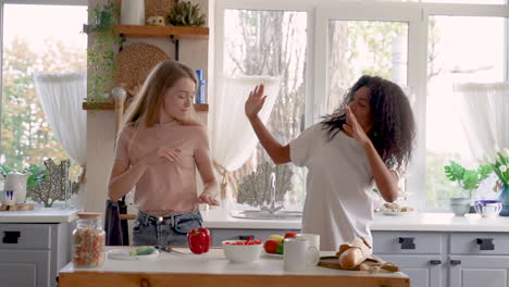 Two-female-friends-dancing-in-the-kitchen.-Black-girl-and-caucasian-young-woman-having-fun-while-cooking.-Medium-shot.