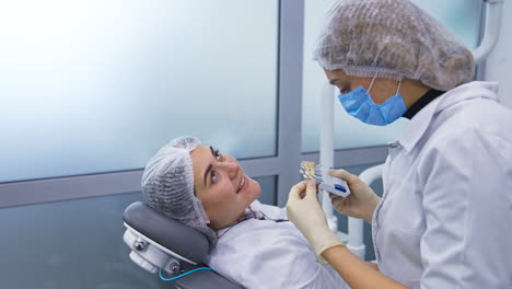 two female students of dentistry department at practice. future dentist chooses the best color species of teeth corresponding to the patient.