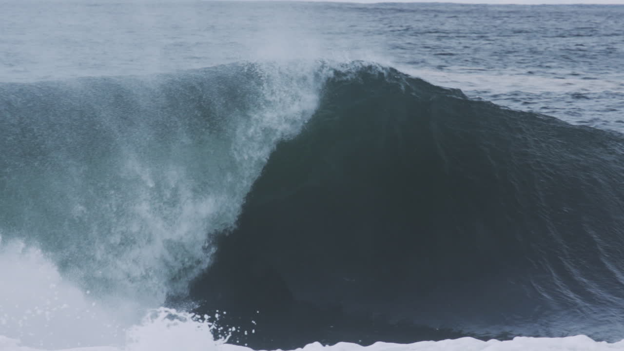 Huge swell rolls with glassy surface as spray flickers off top in slow motion compression