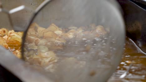 Extreme-closeup-of-a-hot-oil-fryer-with-curly-fried-tornado-potatoes-cooking-and-someone-dipping-a-strainer-in-to-pull-out-fries