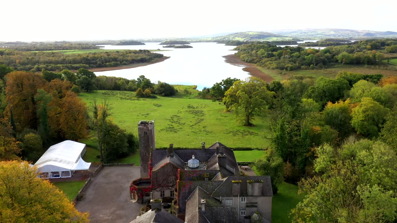Drone panoramic overview of castle structure emerging from vibrant fall trees with soft golden hour light