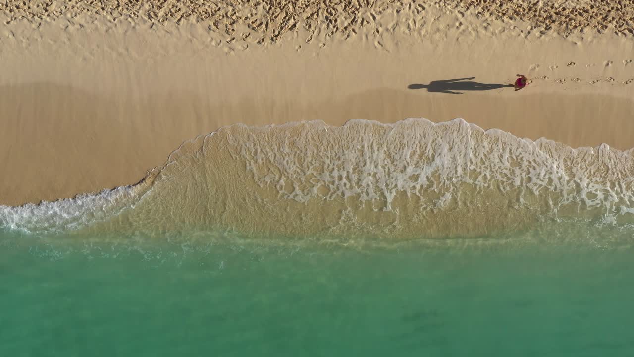 Woman walking along tropical sandy shore of caribbean sea with waves, travel destination, nature background. Aerial top view