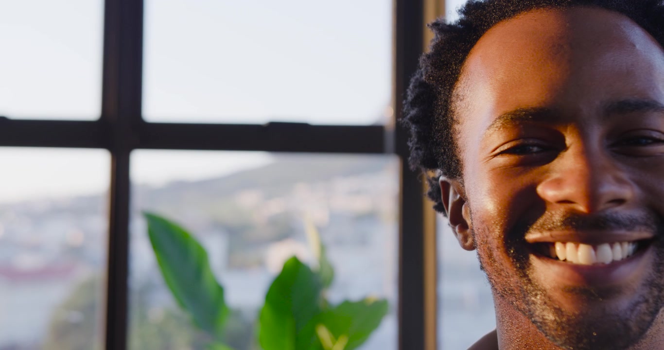 African American man smiling then laughing, responding to off-camera cue at home window, copy space