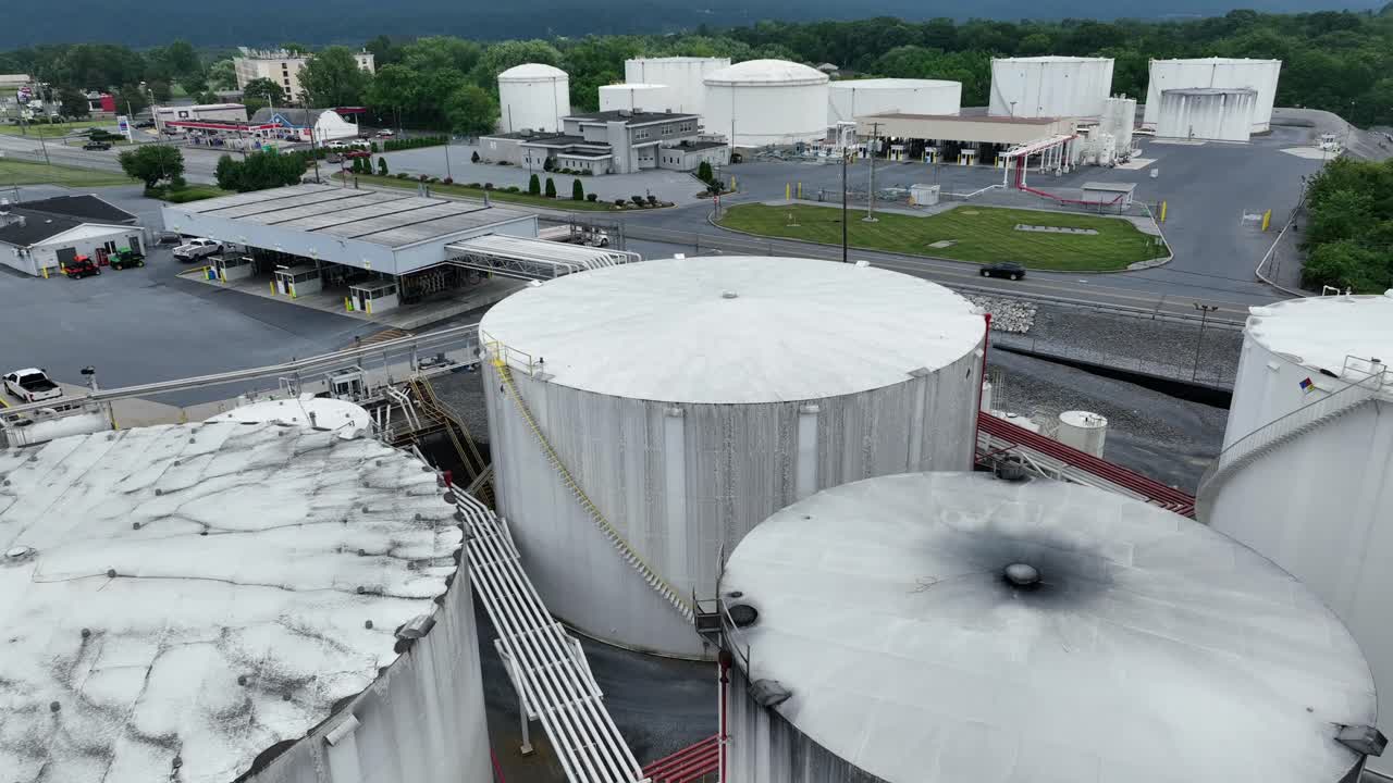Descend drone shot of white storage tanks with fuel and car on street. Fuel terminal in industrial area of American town. Wide shot