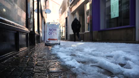 Person-walking-through-back-street-as-snow-melts-and-water-drips