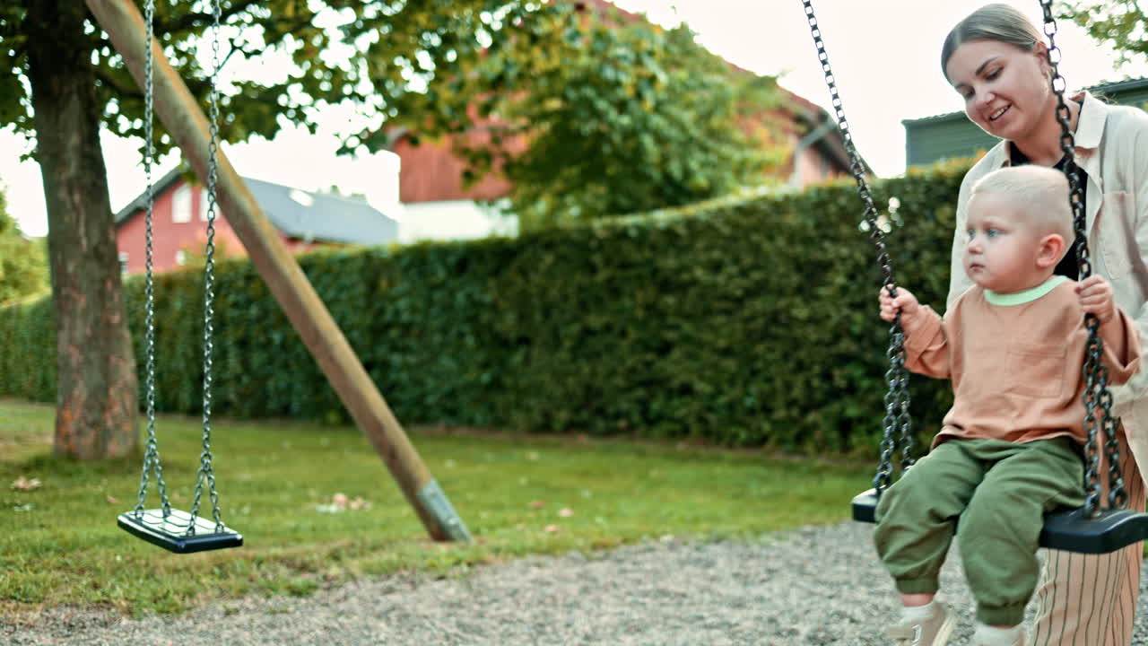 Madre e figlio felici giocano all'aperto nel parco giochi. La mamma fa dondolare il figlio sull'altalena in un parco cittadino. Concetto di maternità felice. Momenti tra mamma e figlio durante una passeggiata. Una madre amorevole trascorre del tempo con suo figlio.