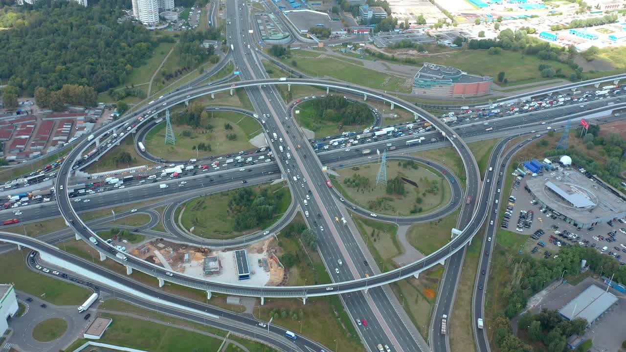volando alrededor de la gran intersección circular con curvas y salidas de trébol. vista aérea de arriba hacia abajo desde el avión no tripulado. atasco de tráfico dentro del área urbana. sombra de las nubes. áreas verdes con hierba y edificios a su alrededor. la cámara se mueve alrededor del punto de vista.