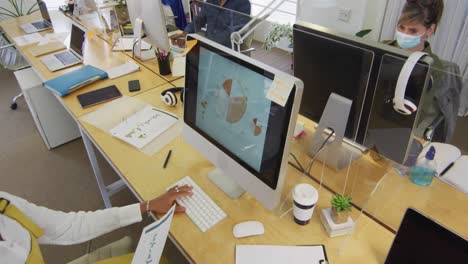 woman wearing face mask passing a document to her colleague at office