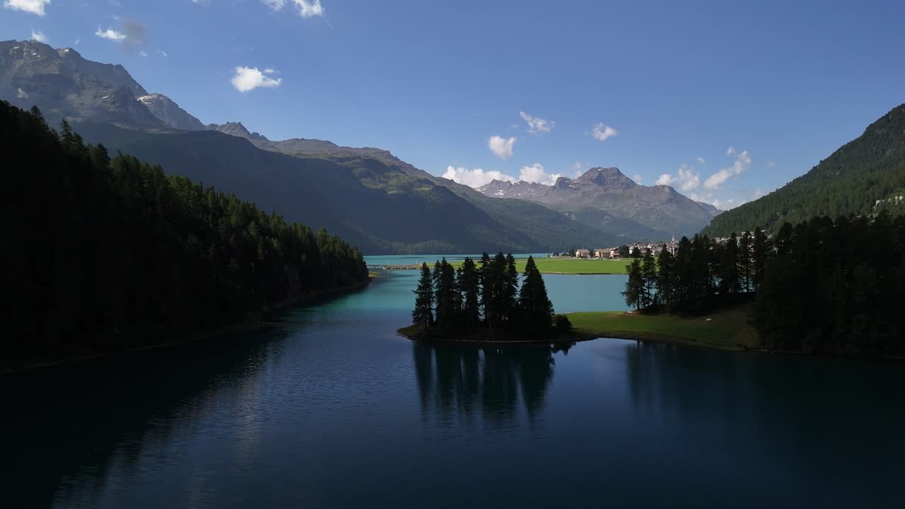 Aerial view of Lake Silvaplanersee in Graubünden, Switzerland, with the shadowed side of the lake unveiling distant mountain ranges and a tranquil residential area nestled along the banks.