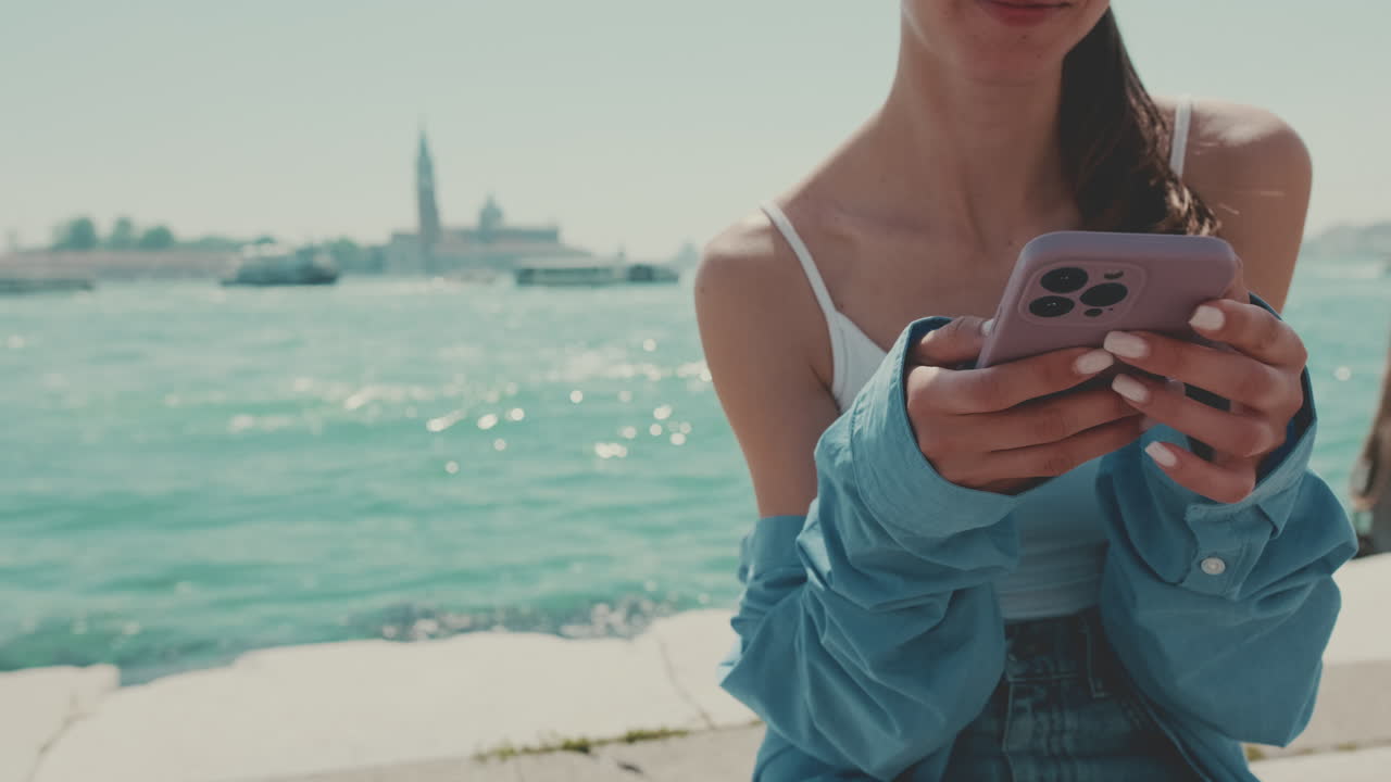 Giovane donna che usa lo smartphone vicino all'acqua in una città europea