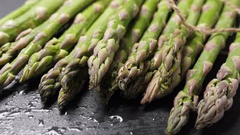 raw green asparagus on wet black slate background