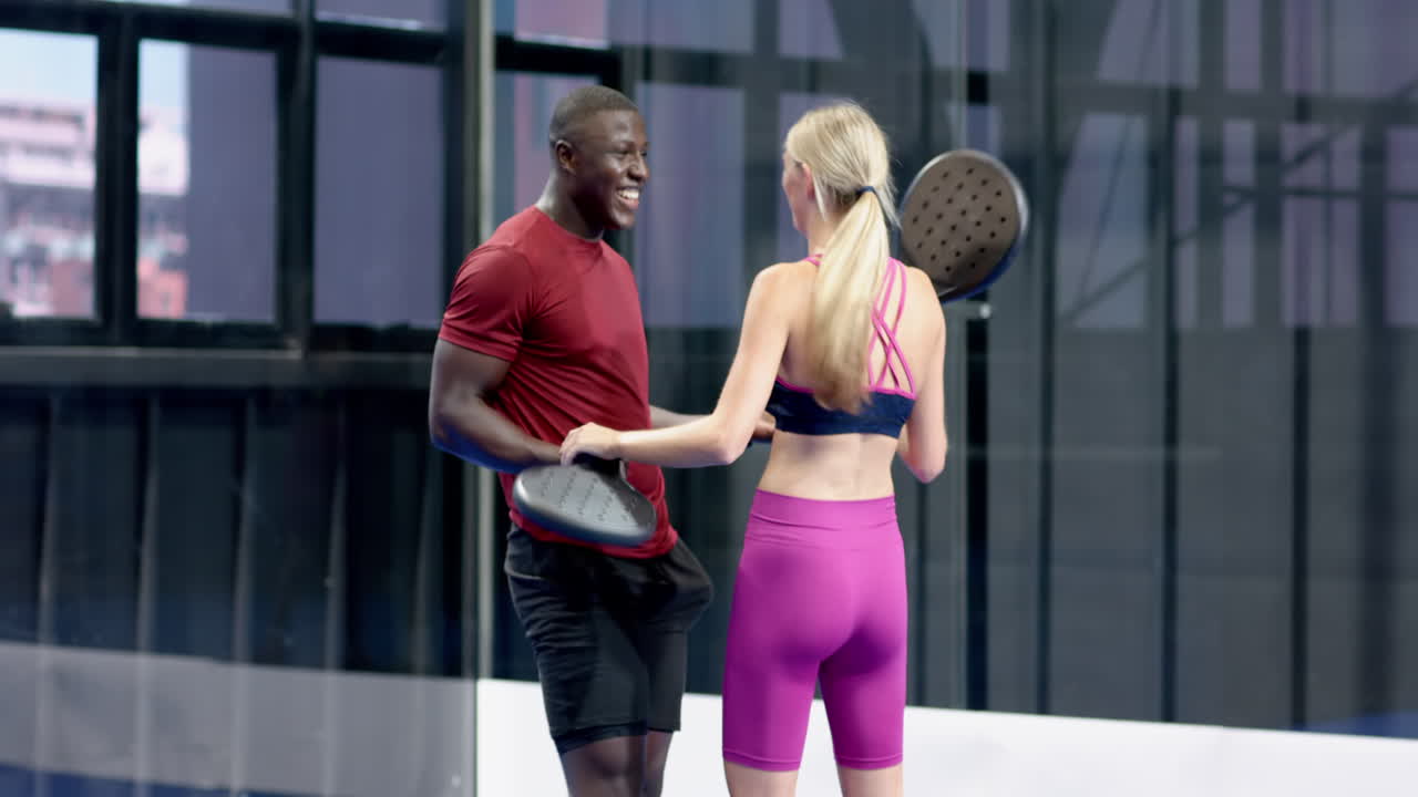 Smiling diverse athletes holding padel rackets, enjoying friendly match on indoor court