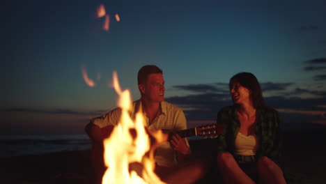pareja tocando la guitarra junto a la fogata en la playa al atardecer