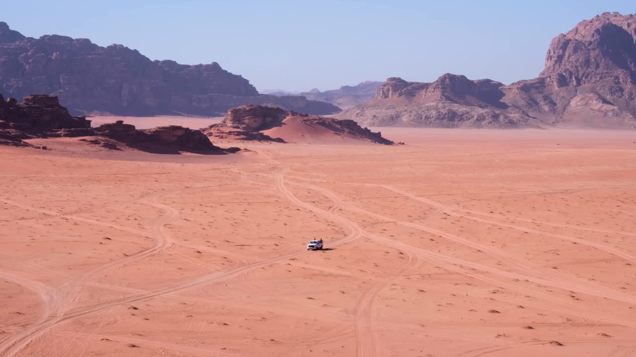 Uzaktaki dağlarla birlikte Ürdün'deki Vadi Rum'da, kırmızı kumlu, geniş ve uzak çöl boyunca izleri takip eden beyaz 4x4 kamyonet