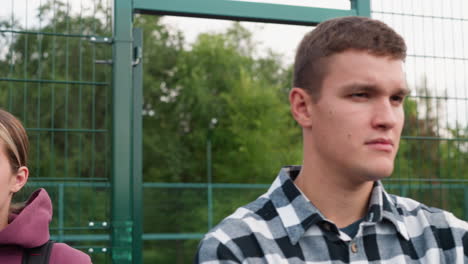 close-up facial view of a young athlete looking focused, standing in a court with green bars and lush trees in the background, embodying determination and readiness