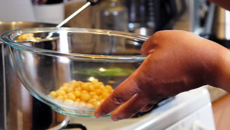 black person's hands seen spooning out chickpeas from the boiling pot into a glass bowl